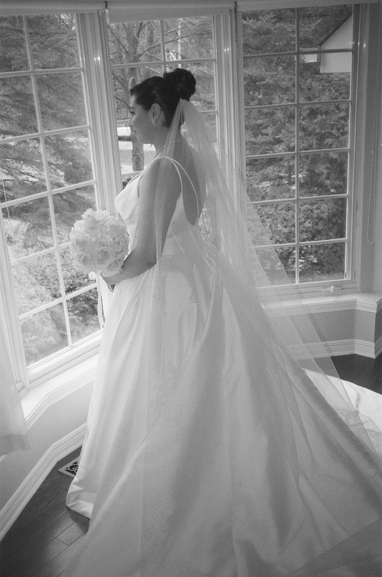 A series of black and white photos showing a bride in a flowing white wedding gown near sunlit windows.