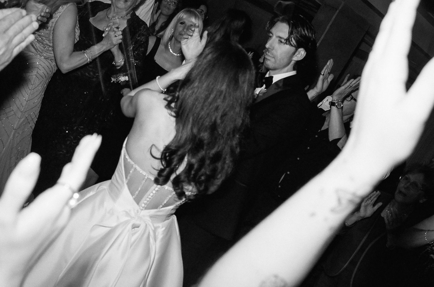 Black and white photo of people dancing with their arms raised at what appears to be a party or nightclub.