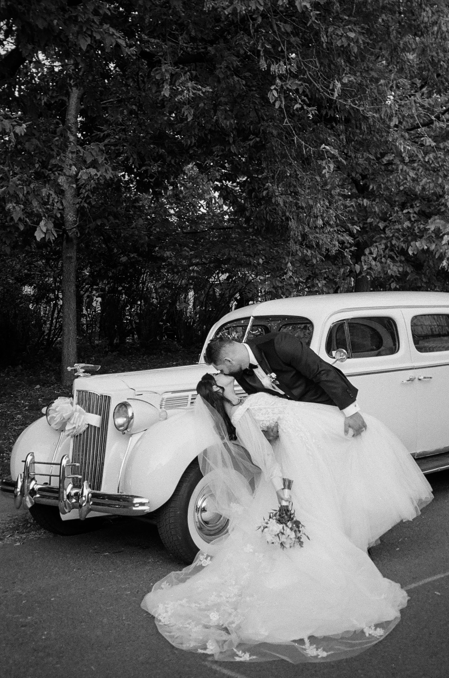 A series of vintage black and white photos showing a bride in a flowing gown posing with classic cars outdoors.