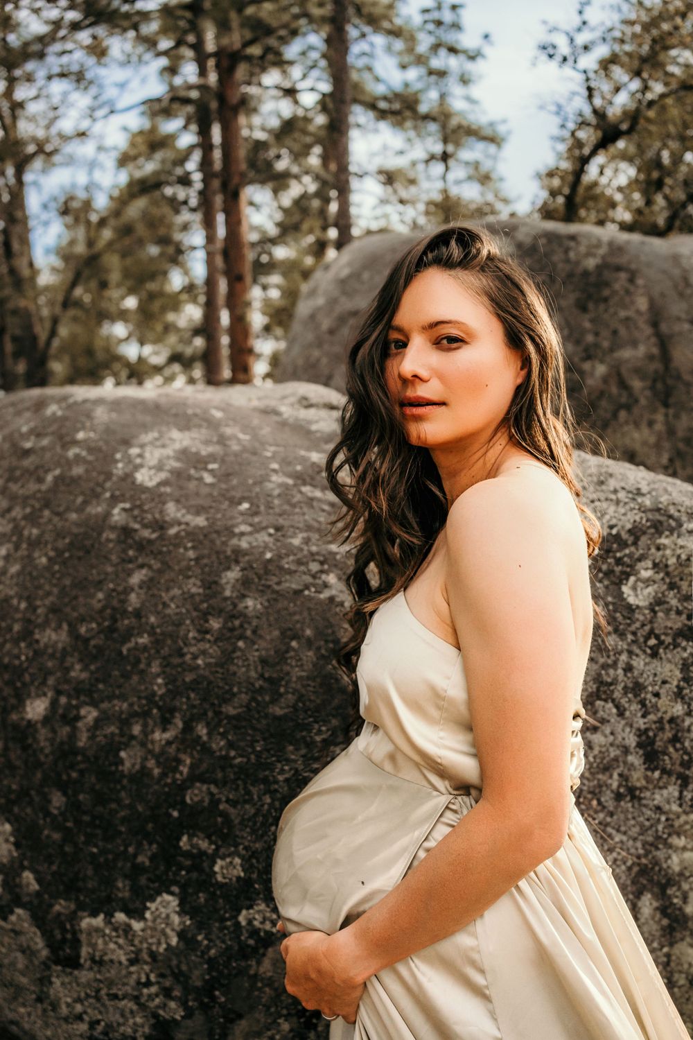 Outdoor maternity portrait against large granite boulders and pine forest backdrop.