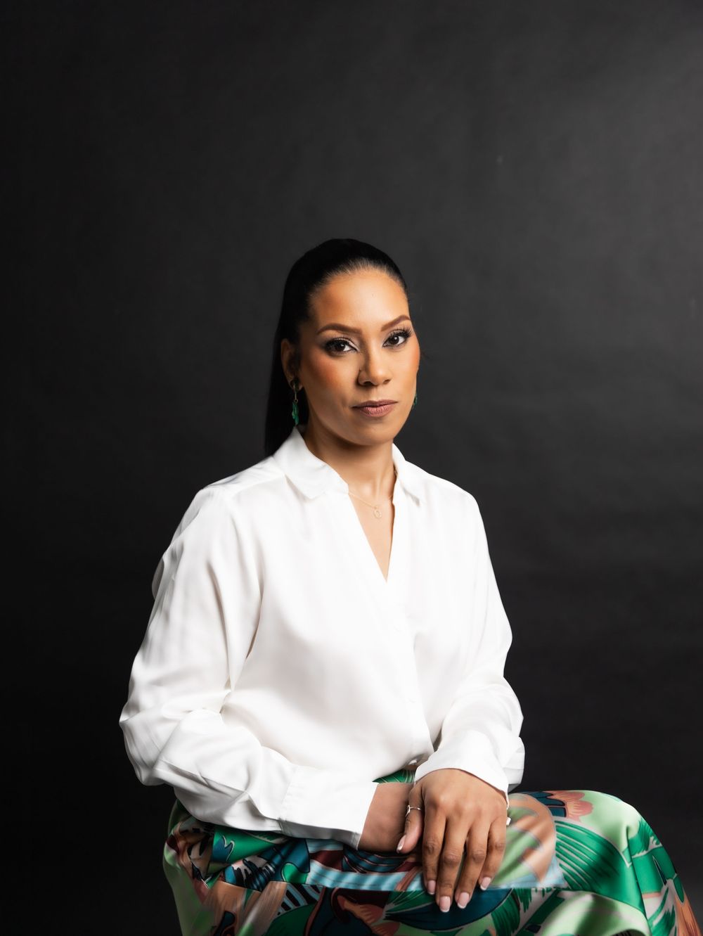 Woman in white blouse and floral skirt poses confidently against dark studio background.