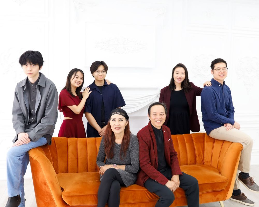 Seven people posing together in a bright studio, sitting and standing around an orange velvet sofa.