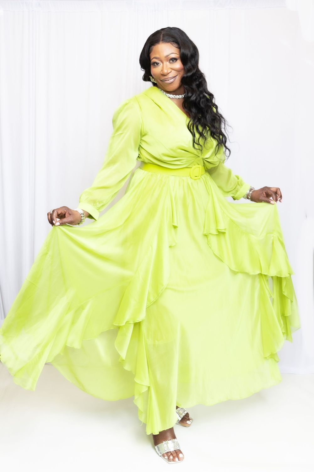 Woman in lime green ruffled maxi dress with long sleeves posing gracefully against white backdrop.