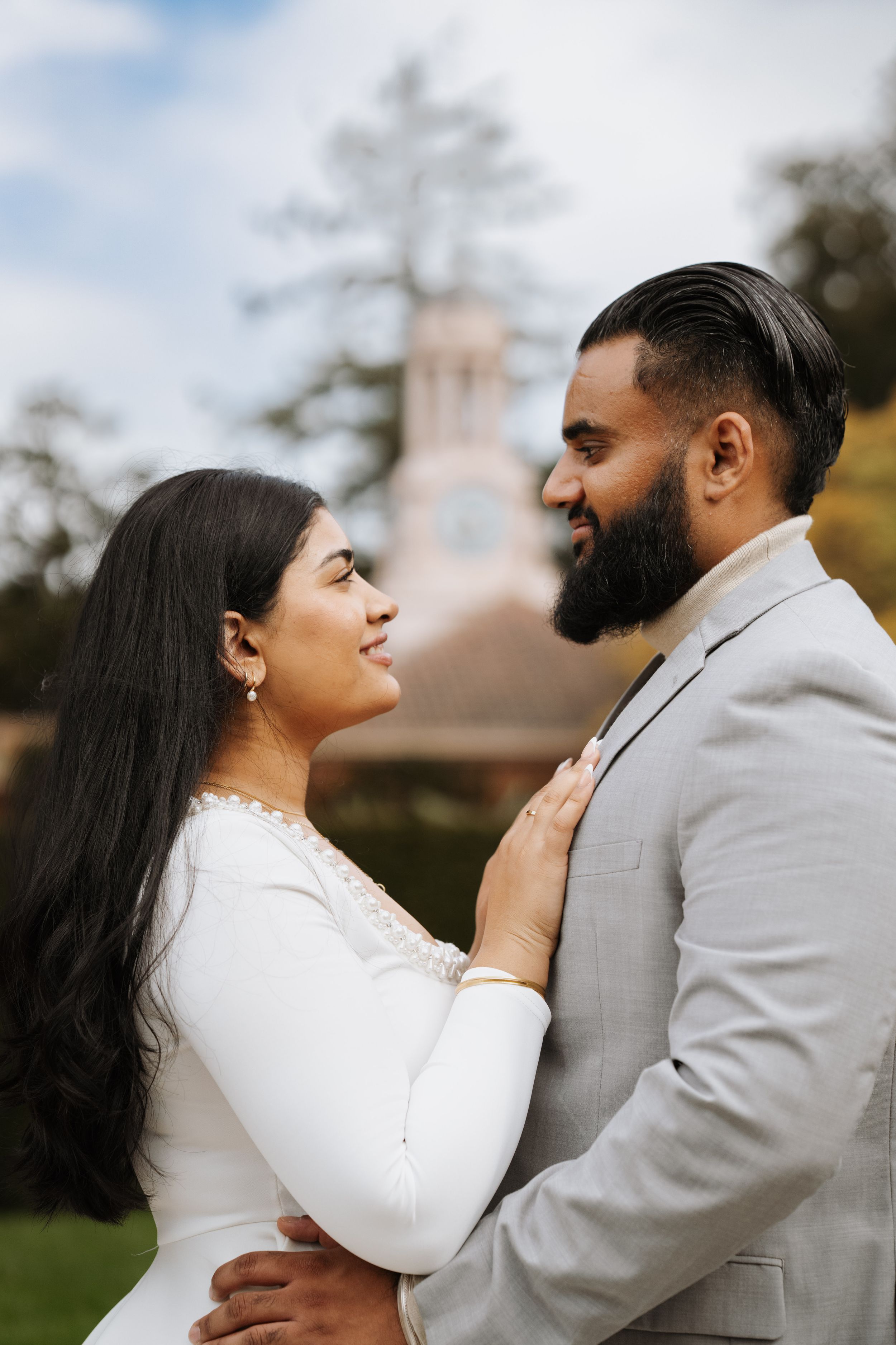 A couple in wedding attire gazes lovingly at each other outdoors, with a blurred building in the background.