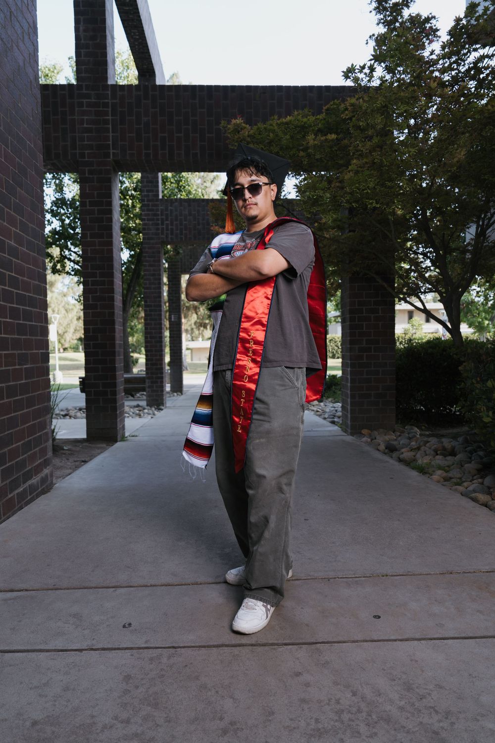 Person standing in sunglasses and casual attire poses confidently under a covered walkway with architectural columns.