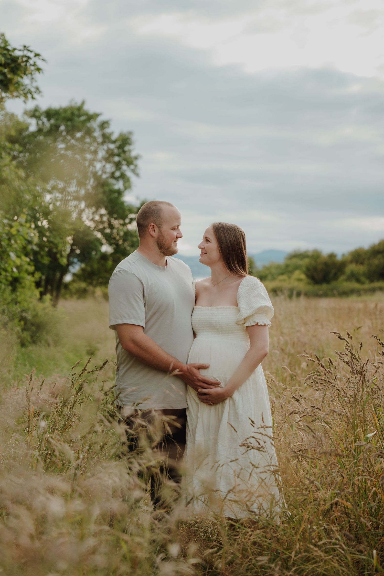 Expectant couple shares a tender moment in a wildflower meadow, cradling pregnant belly outdoors. Victoria, BC, Vancouver Island.