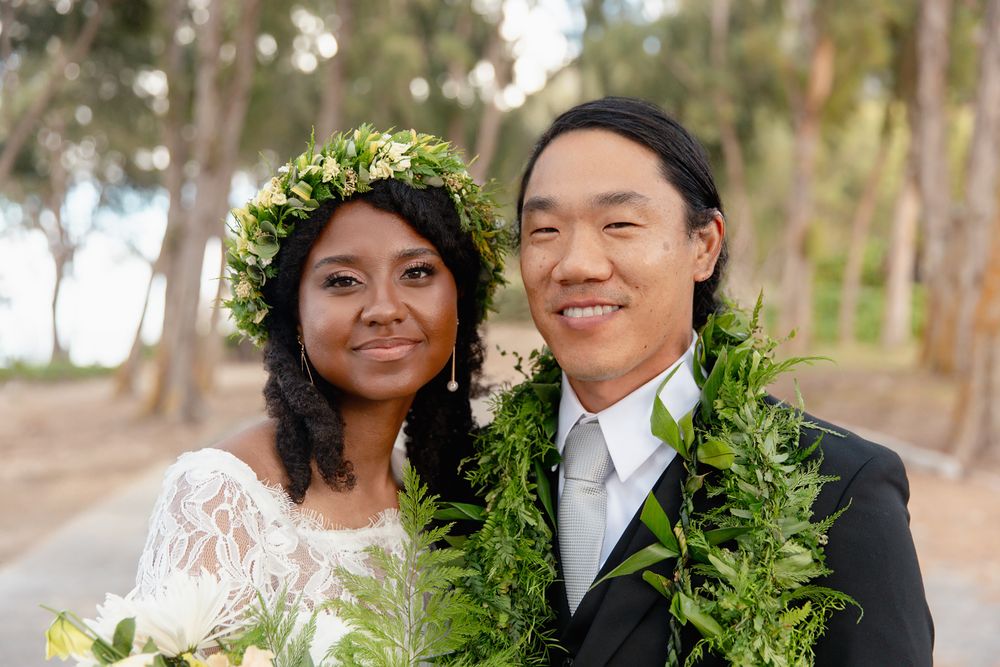 Wedding couple wearing traditional Hawaiian leis and formal attire in a tropical forest setting.