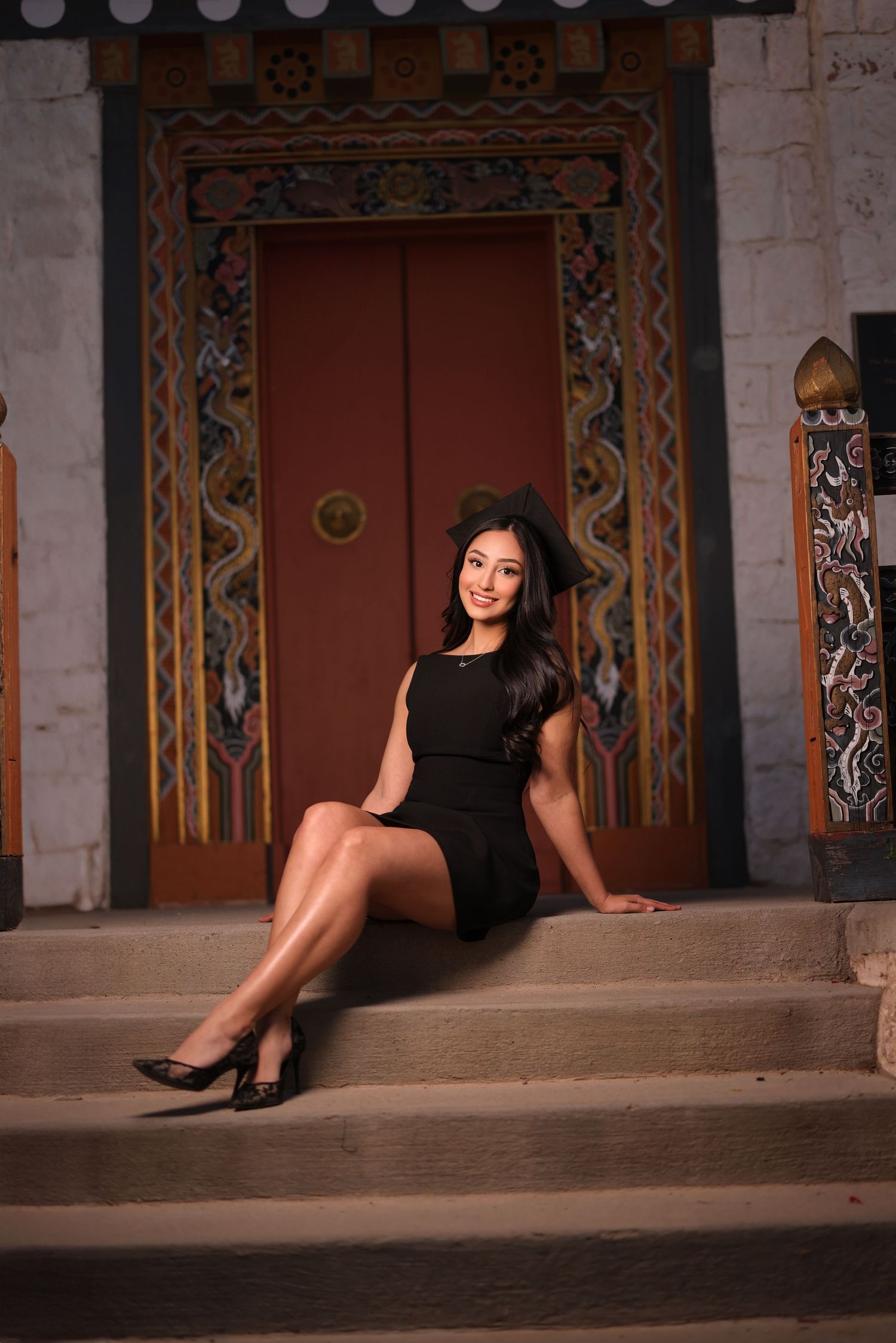 Elegant pose on ornate steps in front of decorative red door.