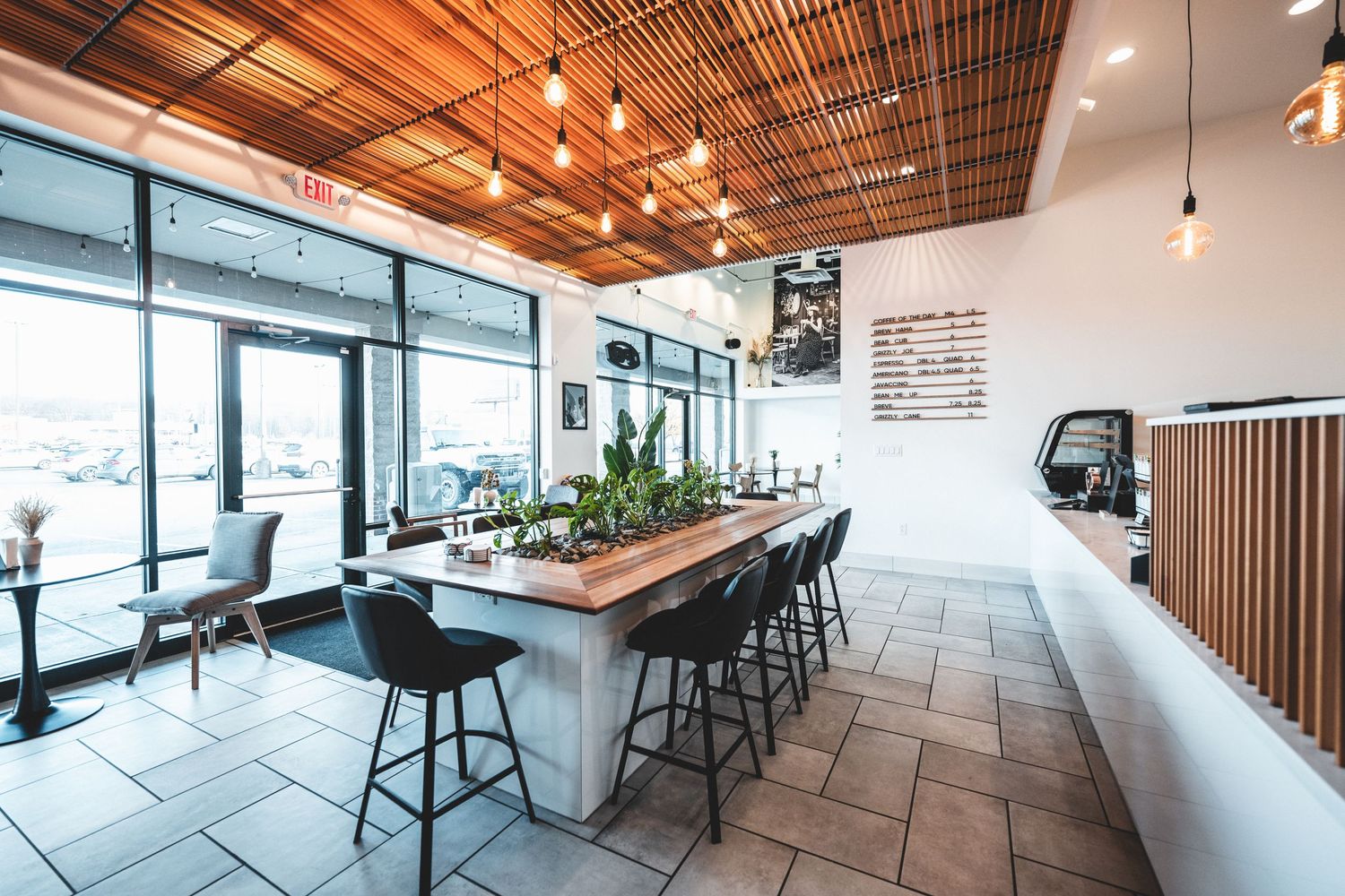 Modern coffee shop interior with wooden ceiling, framed wall art, counter service area and communal table seating.