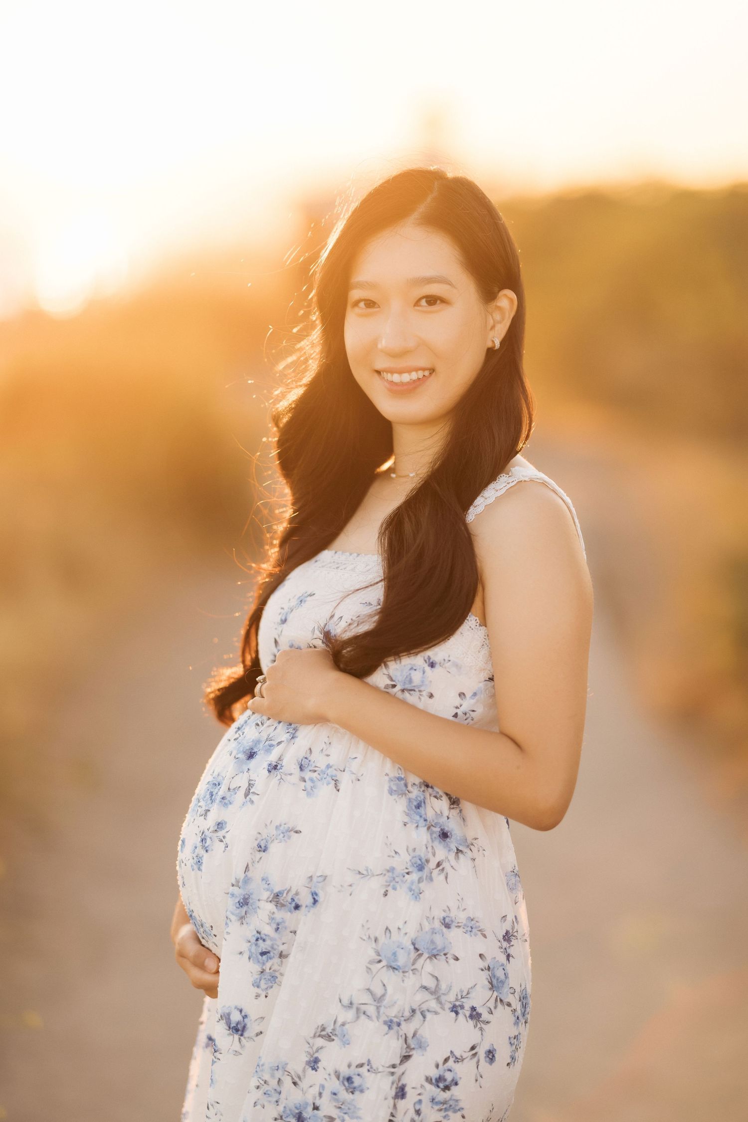 A woman in a floral dress cradles her baby bump during a golden hour photoshoot.