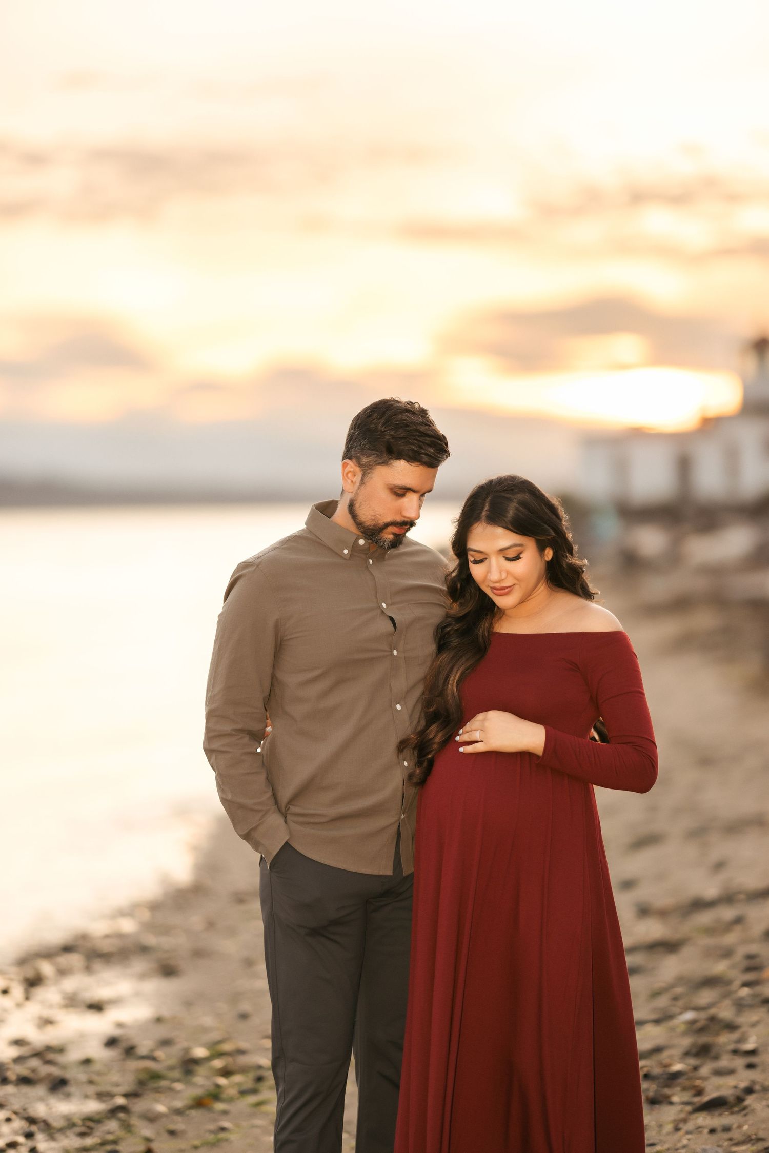 Maternity beach photoshoot at golden hour with couple in coordinated casual outfits.