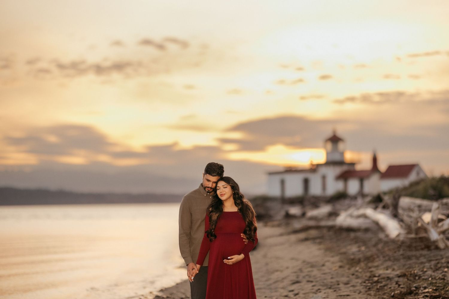 Maternity photo session at sunset near lighthouse with couple in romantic pose.