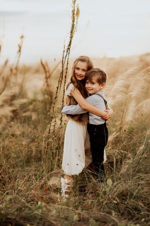 Two young children hugging and smiling in a golden field of tall grass during sunset.