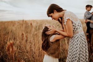A mother tenderly holds her daughter's face in a golden wheat field, sharing a joyful moment outdoors.