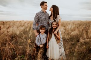 Family of four posing in golden field, parents gazing at each other, children smiling in rustic outfits.
