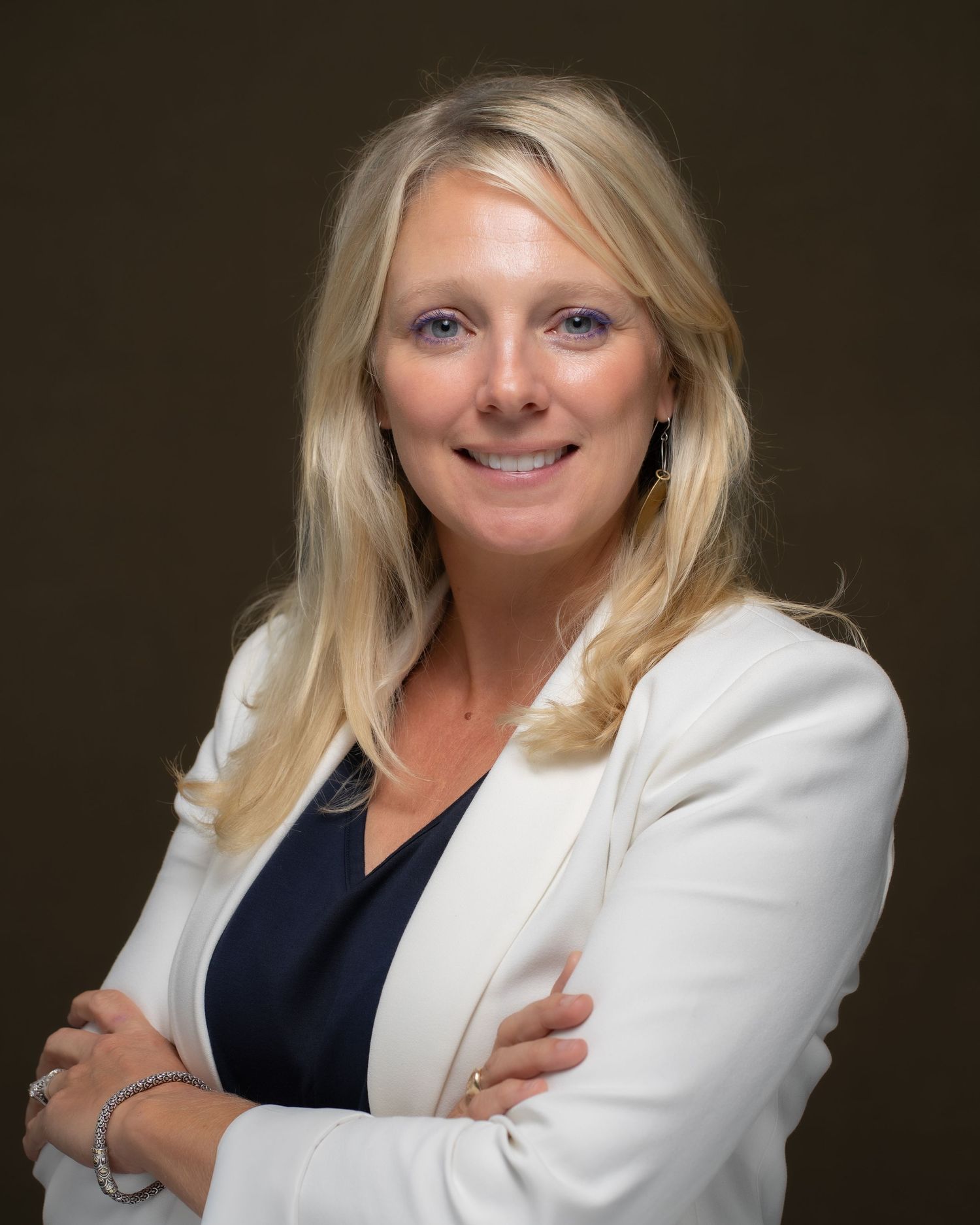 Professional headshot of smiling woman in white blazer with arms crossed, posed confidently