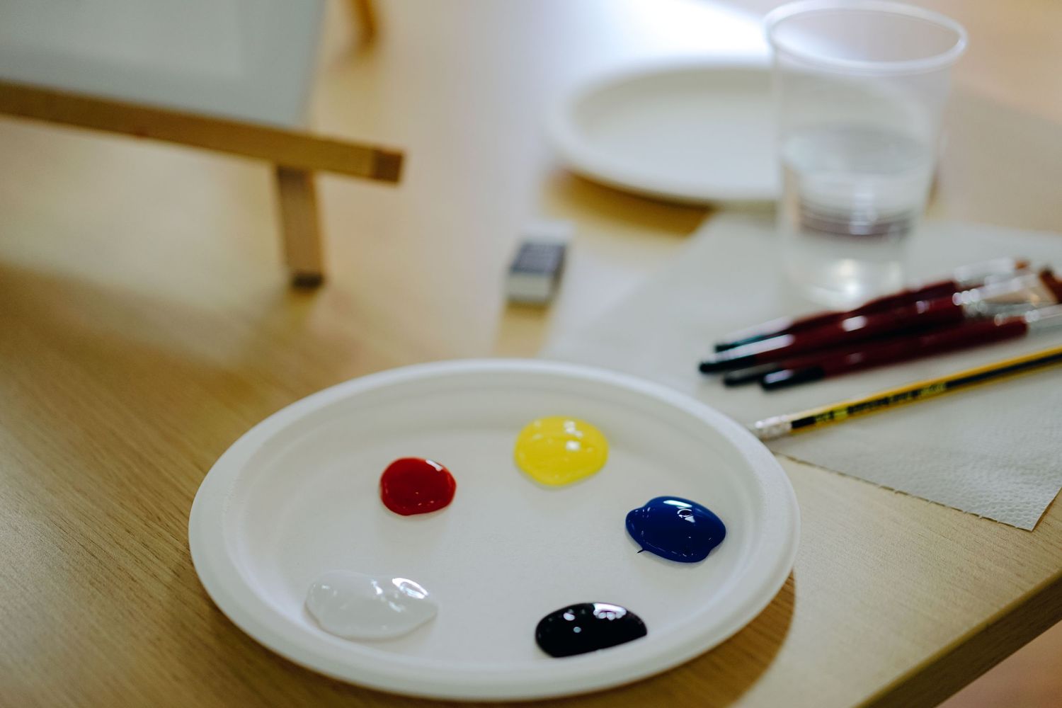 Paint palette with red, yellow, blue and white colors on a wooden table.