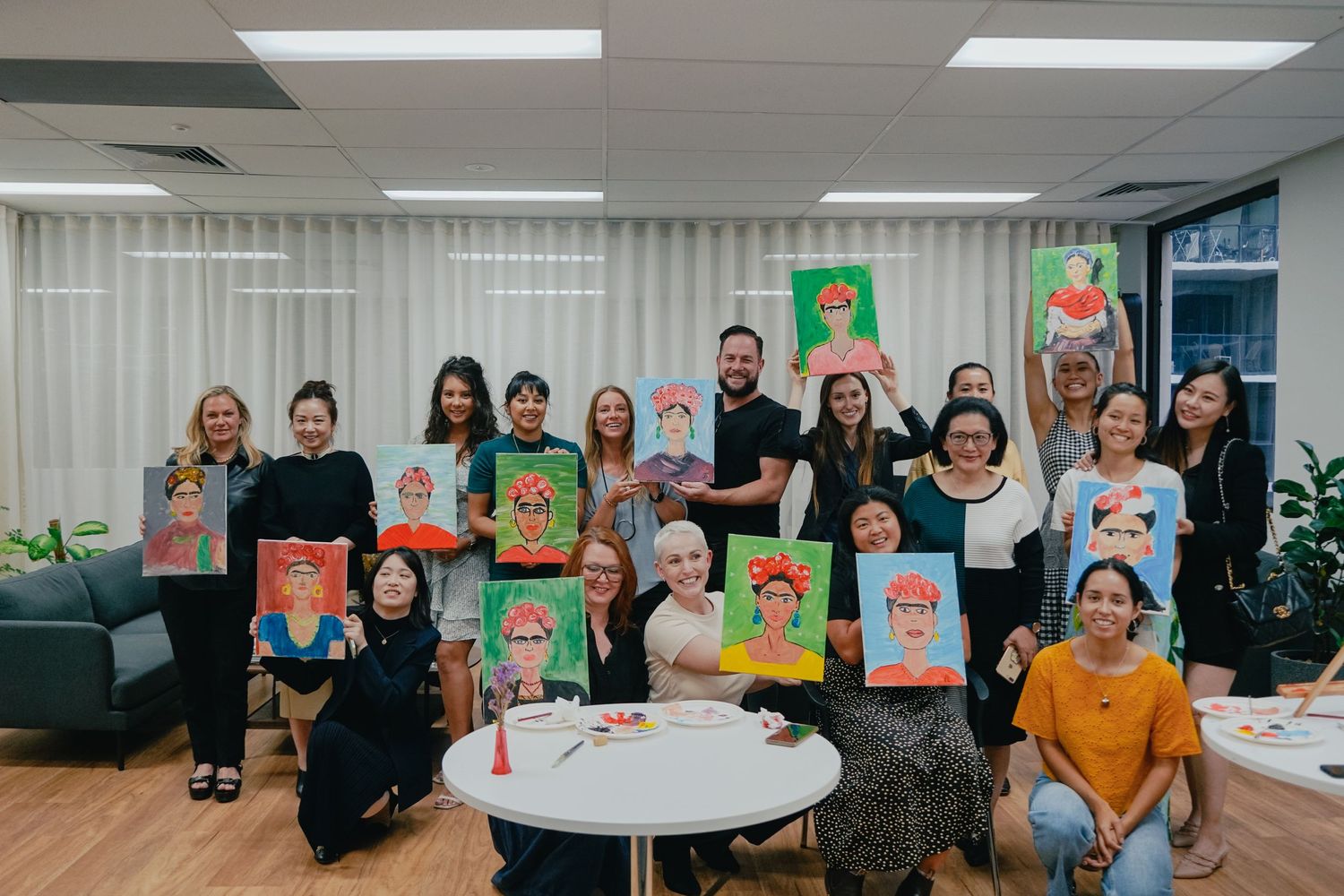 Art class participants showing their colorful portrait paintings in modern classroom.