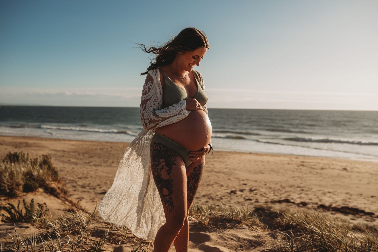 Beautiful beach maternity photoshoot with flowing fabric against ocean backdrop.