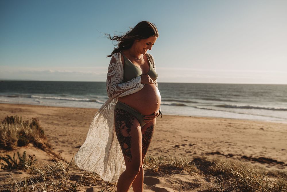 Beautiful beach maternity photoshoot with flowing fabric against ocean backdrop.