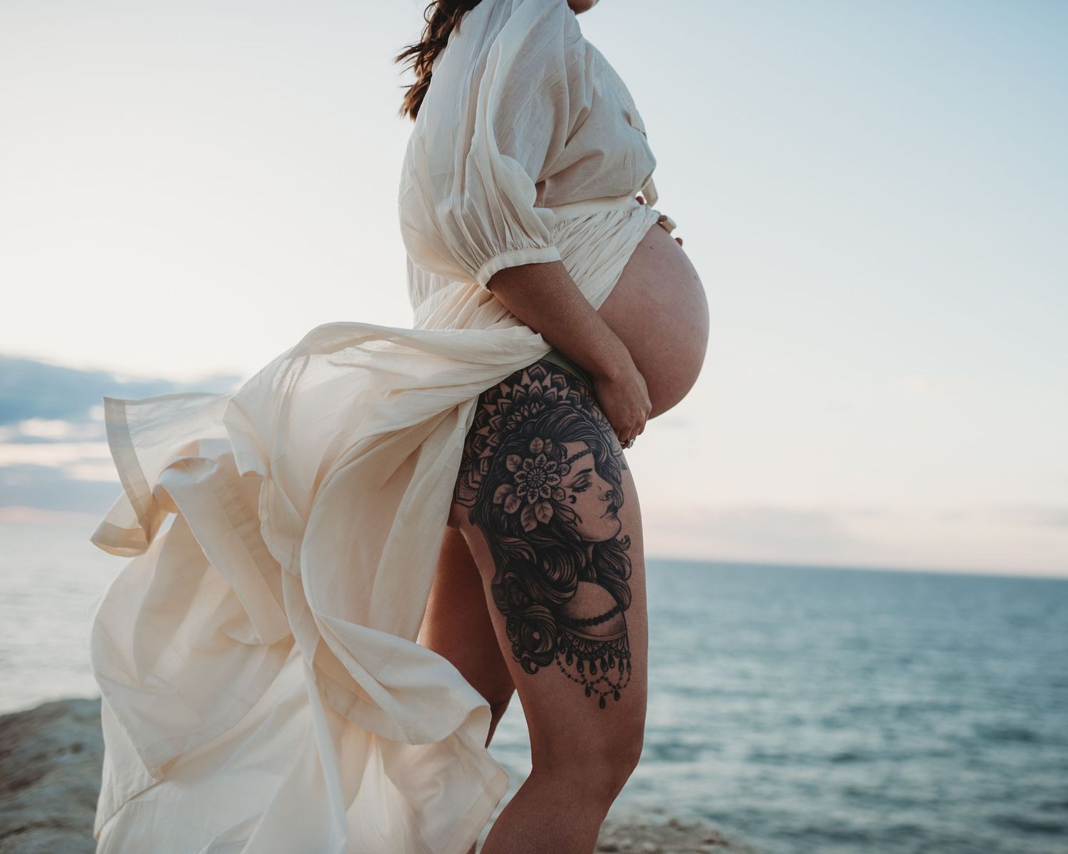 Ethereal beach maternity photos with flowing white dress against ocean waves.