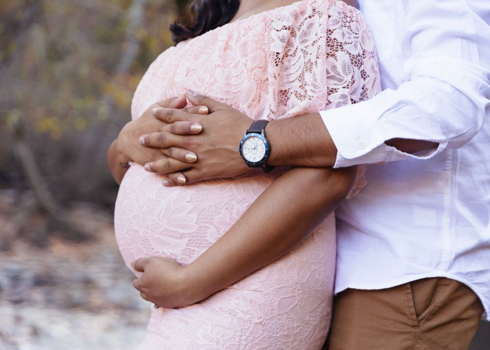 Close-up of hands embracing a pregnant belly in pink lace dress.