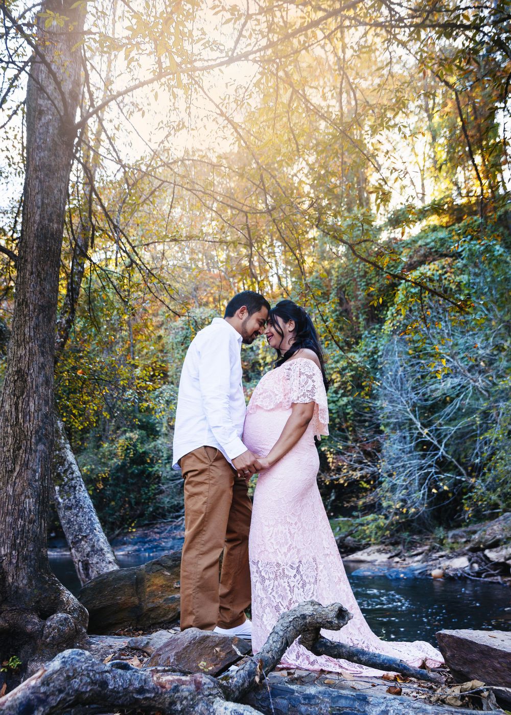 Romantic maternity photo of couple standing by a stream in autumn woods.