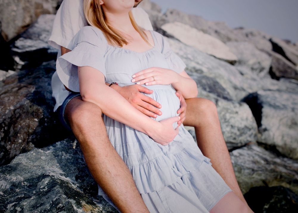 Intimate maternity portrait on rocky beach with soft lighting.