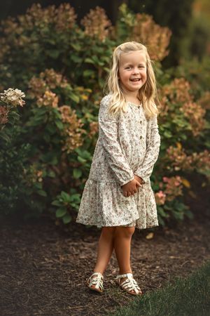 A child in a floral dress plays outdoors near autumn foliage in a series of candid moments.