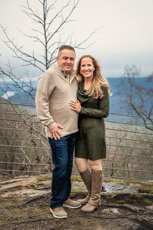 A couple shares a joyful moment together on a scenic mountaintop overlook during an autumn day.