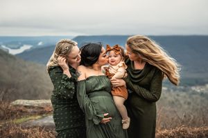 A group of women in warm clothing shares an intimate moment on a mountaintop with scenic views in the background.