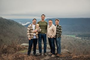 A group stands together on a mountain overlook with sweeping valley views and blue skies in the background.