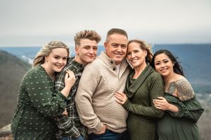 Multi-generational family wearing warm sweaters embraces while standing together at a beach on an overcast day.