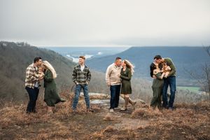 Several couples from an extended family share romantic embraces while standing on a hilltop overlook with mountain views in the background.