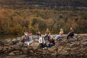 Extended family group sitting on rocky terrain during autumn enjoying sunset views over a scenic valley landscape.