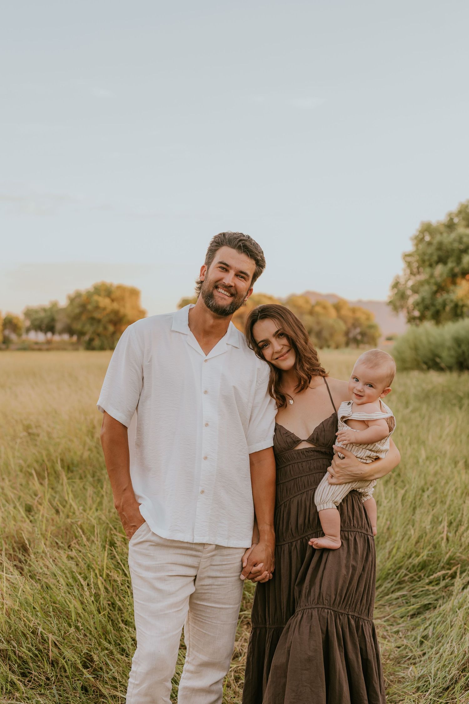 Family poses together in tall grass field during golden hour.