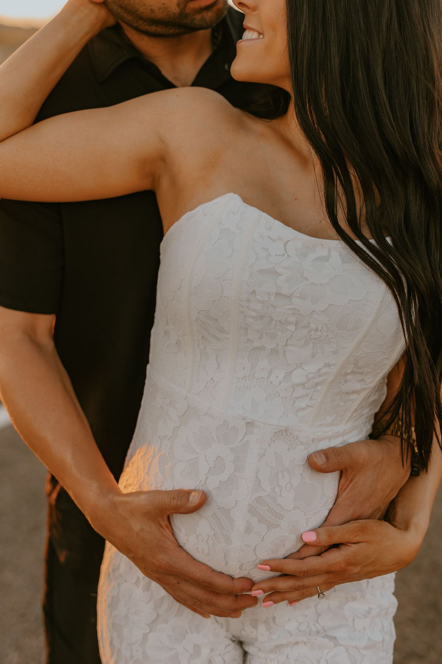 Intimate couple in tender embrace with woman wearing white lace dress during golden hour photography session.