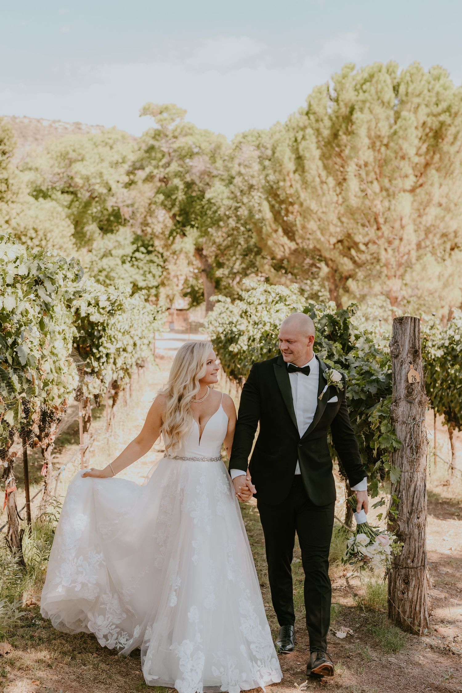 Wedding couple walking and laughing together through vineyard.