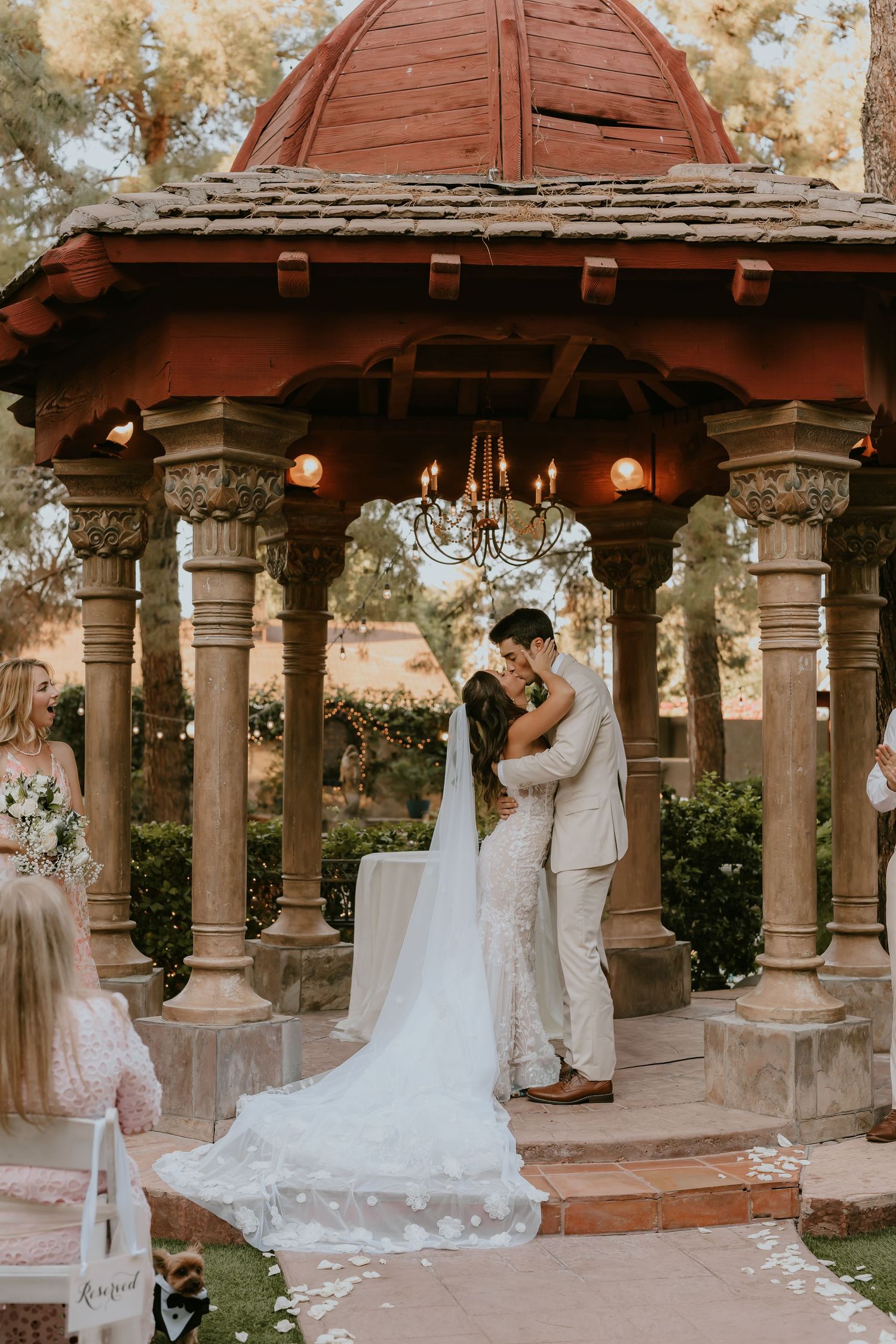 Wedding couple shares intimate moment under ornate red-roofed gazebo.