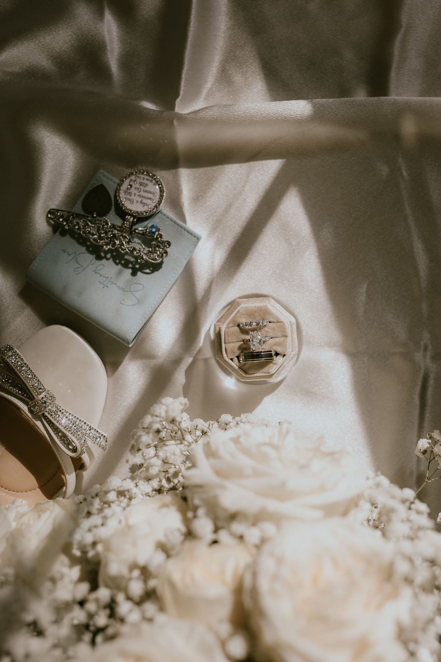 Wedding details flatlay with perfume bottles and white roses in soft lighting.