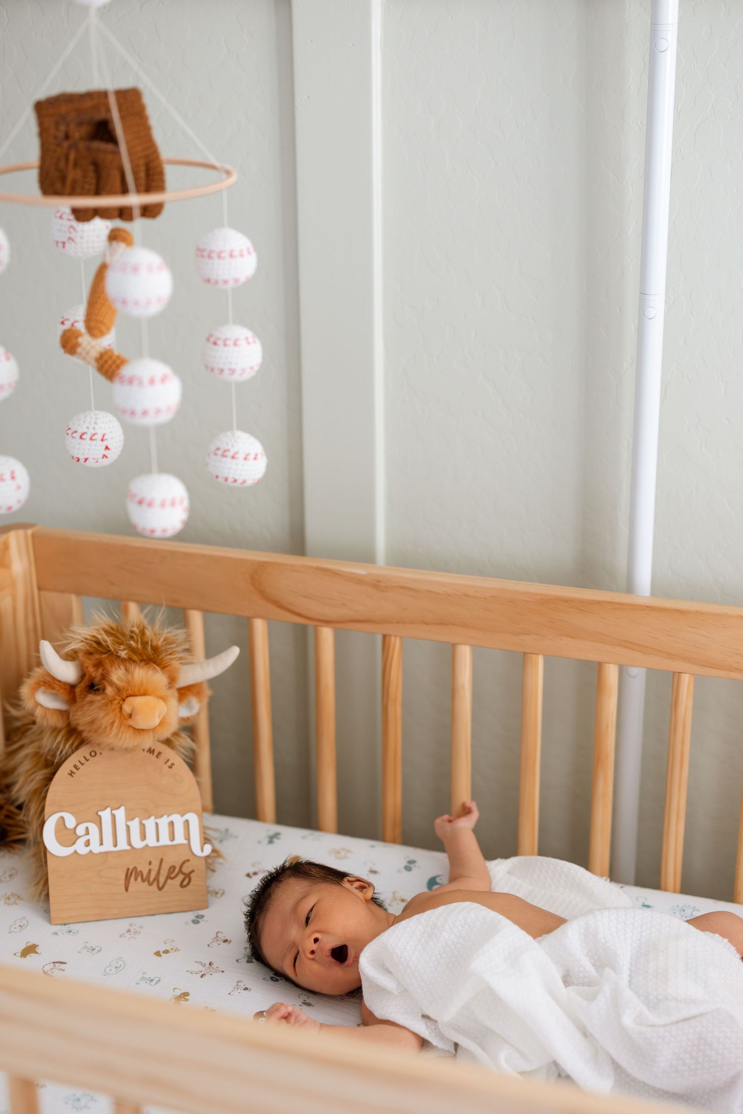 Baby crib with baseball mobile and plush animal toy decor.