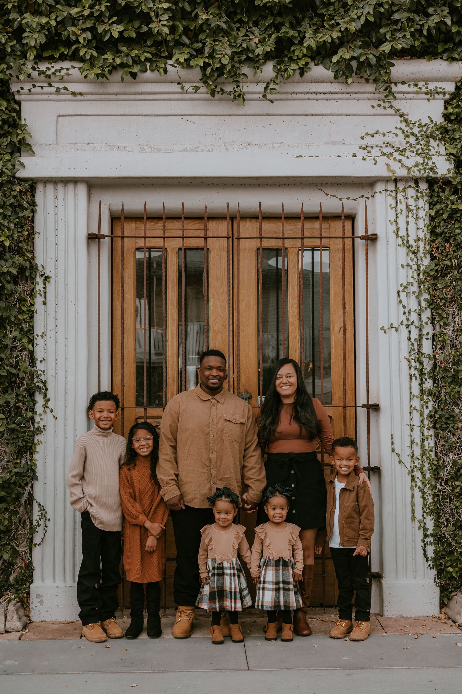 Family poses in front of white colonial doorway with ivy growing around pillars.
