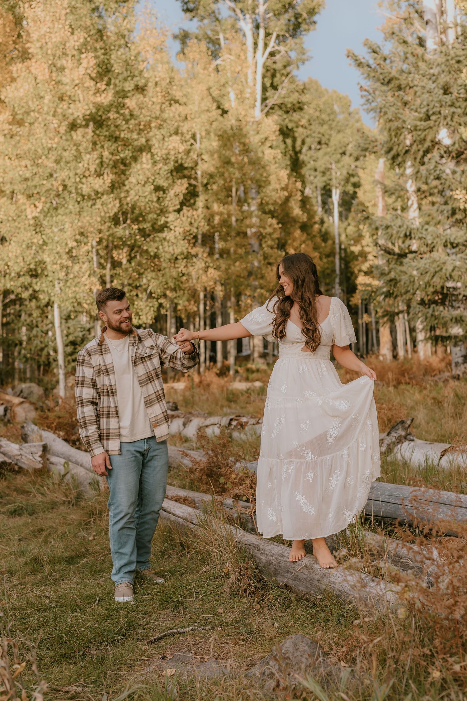 A couple enjoys an autumn day walking among golden aspen trees in a rustic outdoor setting.