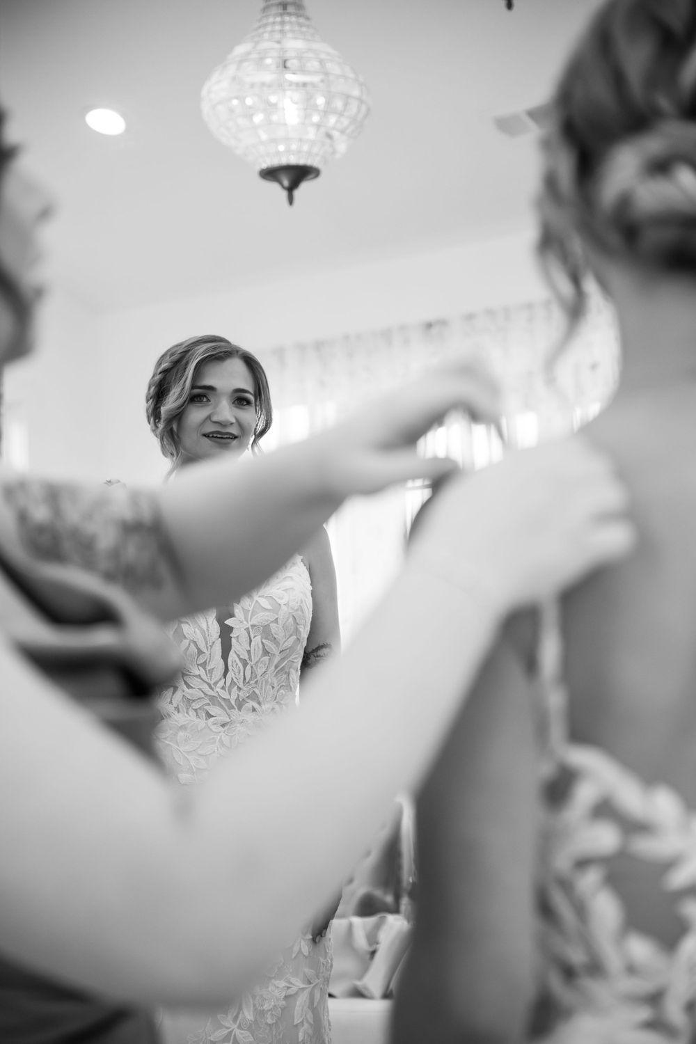 Black and white candid wedding preparation moment under a crystal chandelier.