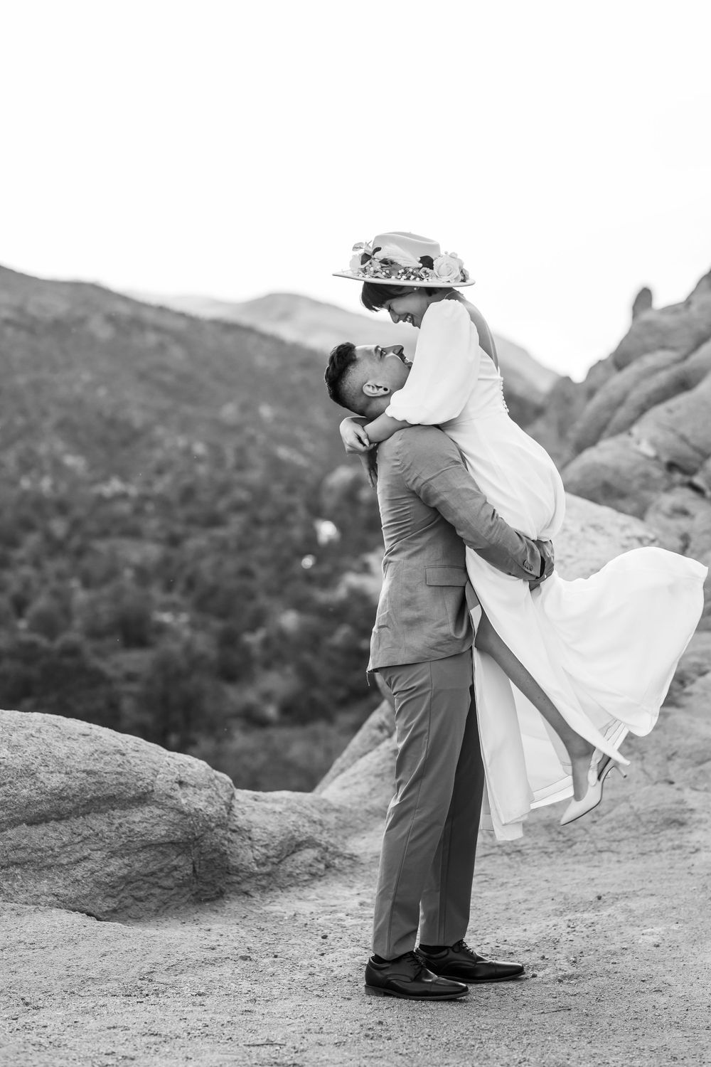Black and white photo of a romantic lift pose on a mountain trail during a wedding photoshoot.