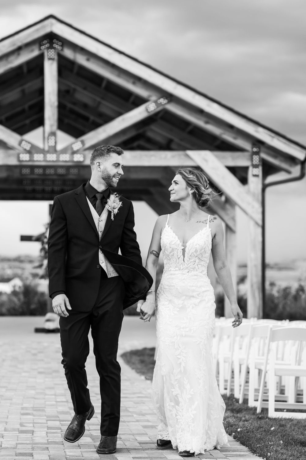 Black and white photo of couple in wedding attire walking under covered outdoor venue.
