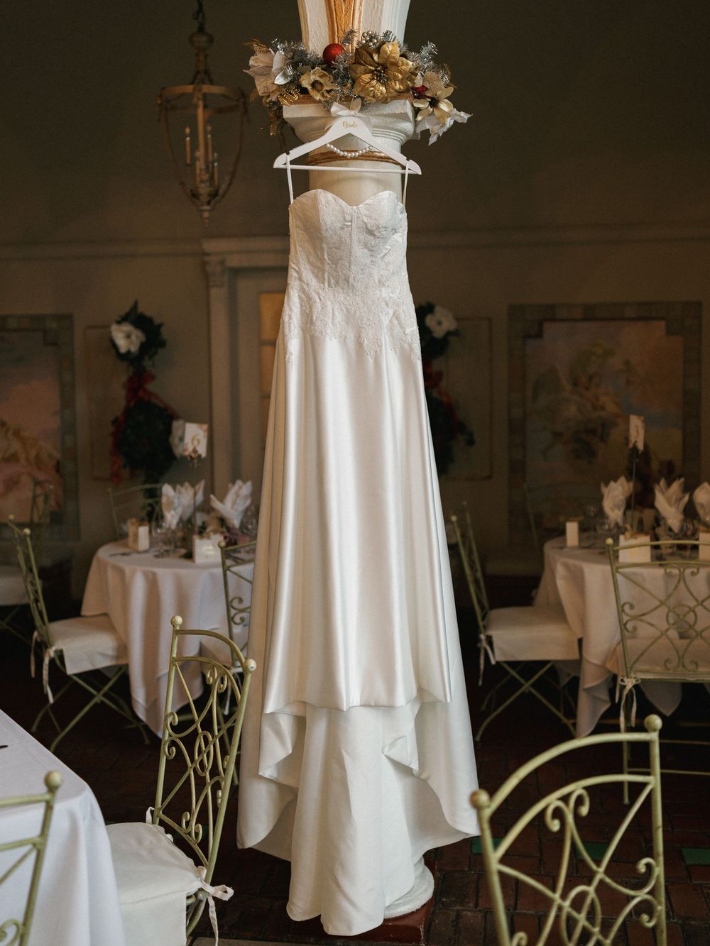 A series of elegant white wedding dresses displayed on hangers in a dimly lit room with decorative floral arrangements.