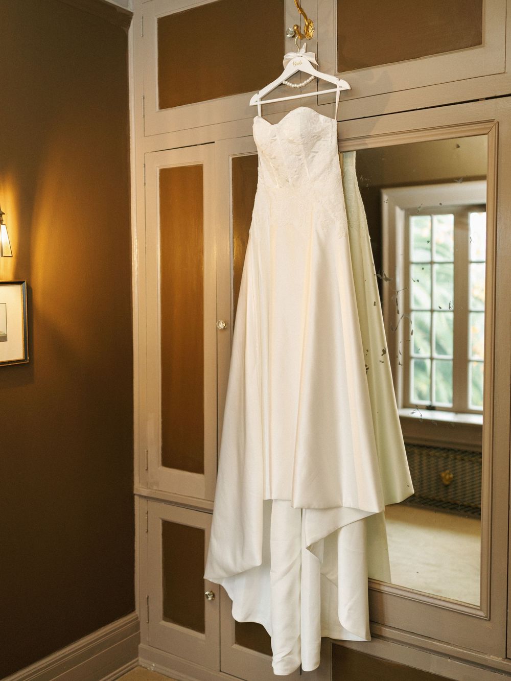 White wedding dress hanging on display in a room with brown walls and white trim molding.
