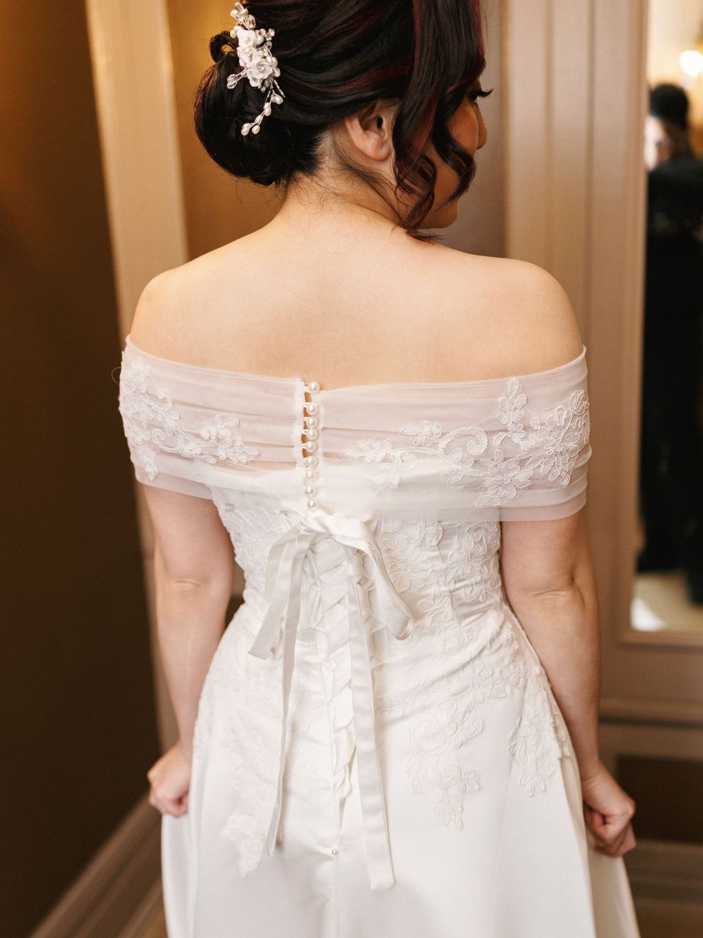 Back view of white wedding dress with delicate off-shoulder lace detail and button closure.