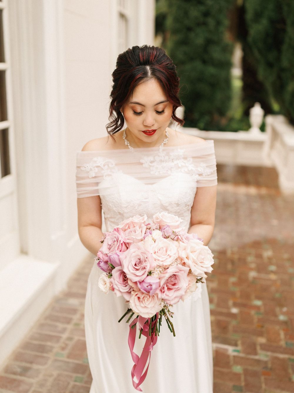 A beautiful pink rose and peony bouquet with mauve ribbons is showcased against a white dress.